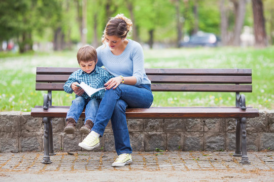 Mother and son sitting on a bench in a park and reading a book