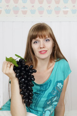 Young beautiful woman smiles and holds black grape in white room