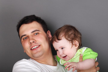 Young happy father holds his little son in green clothes