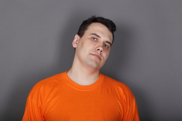 Handsome young man orange t-shirt in grey studio looks at camera