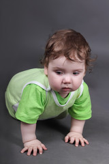 Handsome little baby boy in green crawls on floor in grey studio