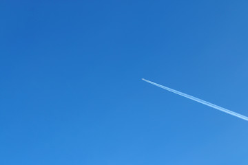 Aircraft flying high in blue sky reserves white trail of engines