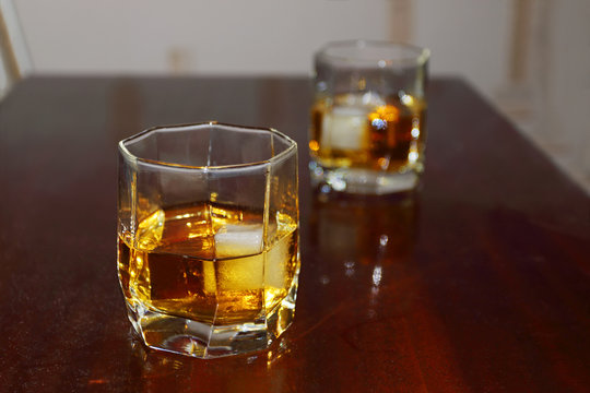 Two glass cup with whiskey and ice on wooden table 