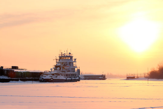 Little ship in frozen river on background of beautiful sunset