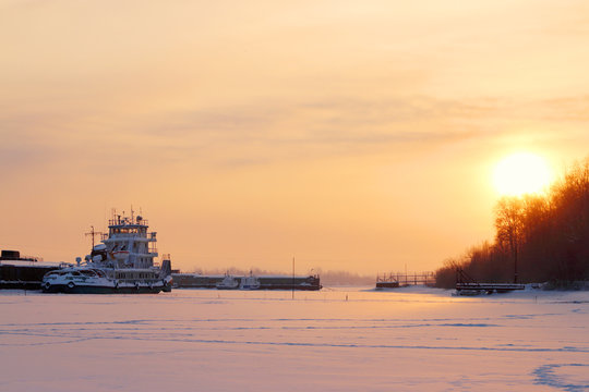 Beautiful sunset with yellow horizon over ship in frozen river 