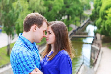 Young woman and man in blue touch noses in summer park
