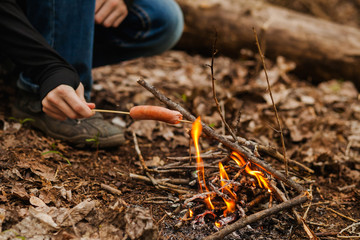 the boy fries sausage on a fire