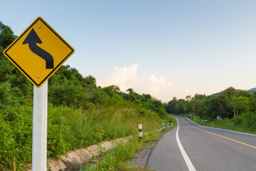 Winding yellow traffic sign against winding road 