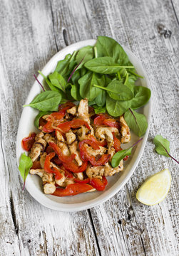 stir fry of chicken breast and sweet red pepper and fresh spinach on a light wooden background