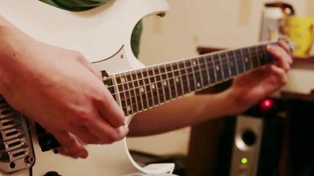 Hands of young man playing modern white guitar at home
