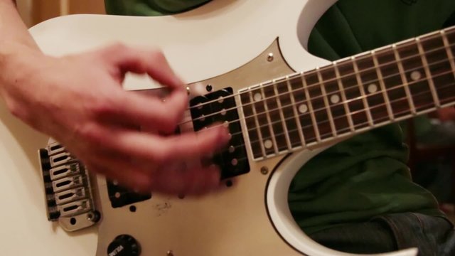 Hands of young man playing white guitar with mediator at home
