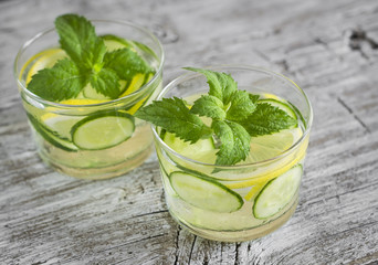 Lemonade with cucumber, lemon, mint and ginger in glass cups on a wooden surface