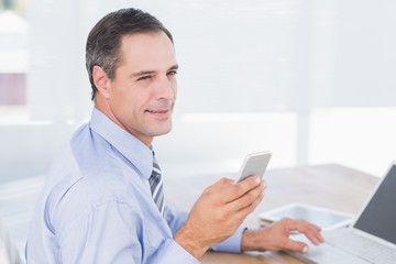 Smiling businessman sending a text at his desk