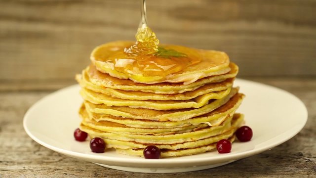 honey is poured on a stack of pancakes on wooden background. Breakfast
