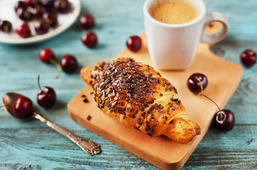Tasty breakfast with fresh croissant, coffee and cherries on a wooden table, selective focus on croissant