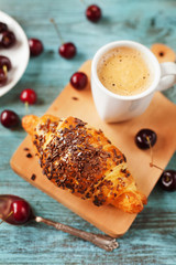 Tasty breakfast with fresh croissant, coffee and cherries on a wooden table, selective focus on croissant