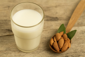 peeled almonds in a spoon c leaves and a glass of milk on wooden table