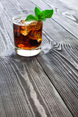 Glass of cola with ice and fresh mint on wooden table.