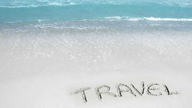 Word TRAVEL written on the sand and waves splashing the beach, crystal clear water.. Waves do not wash off the text.