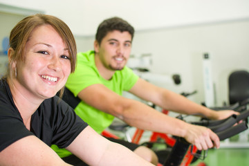 Fototapeta na wymiar man and woman with stationary bicycle in gym 