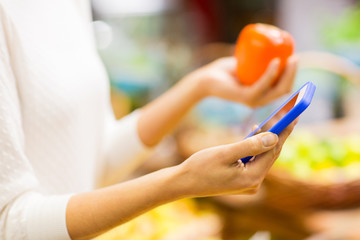 woman with smartphone and persimmon in market