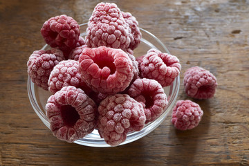 Tiefgefrorene Himbeeren in einer Glasschale auf Holztisch