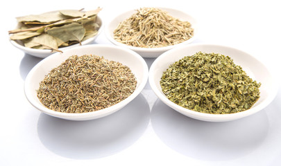 Rosemary, parsley, bay leaves and thyme in white bowl over white background