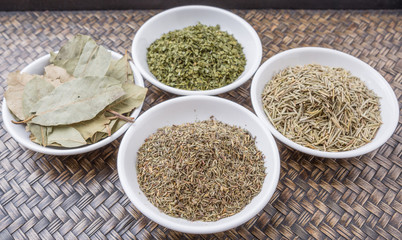 Rosemary, parsley, bay leaves and thyme in white bowl over wicker background