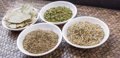 Rosemary, parsley, bay leaves and thyme in white bowl over wicker background