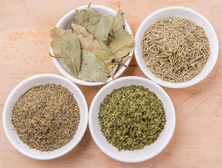 Rosemary, parsley, bay leaves and thyme in white bowl over wooden background