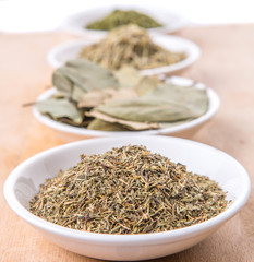 Rosemary, parsley, bay leaves and thyme in white bowl over wooden background