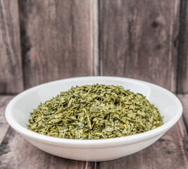 Dried parsley herb in white bowl on weathered wooden background