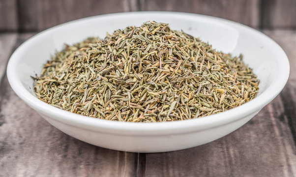 Dried thyme herbs in white bowl over weathered wooden background