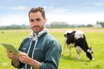 Portrait of a young attractive farmer in a pasture with cows