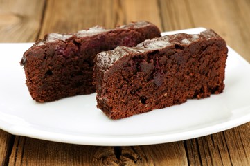 Two pieces of dark chocolate cake with cherries in white plate