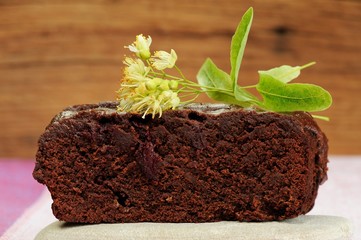 Dark chocolate cake with linden blossoms on wooden background