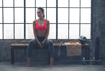 Fit woman sitting on bench in workout gear listening to music