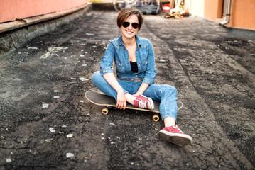 portrait of brunette girl, hipster woman with skateboard, sunglasses and jeans outfit.
