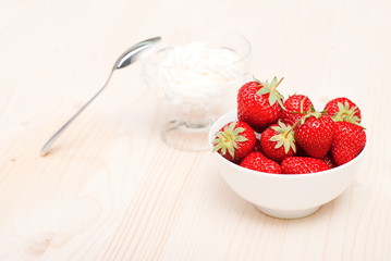 Strawberries in a white bowl on a light table, on the background