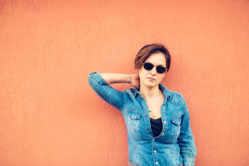 Happy hipster girl posing, against orange background on city streets. Urban lifestyle of contemporary world