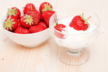 Bowl with cream and two ripe strawberries on the background of a