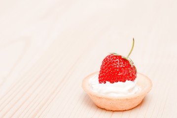 Tartlets with cream and strawberries on a light table, side view
