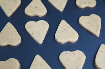 Heart shaped raw dough cookies with caraway on metal baking tray