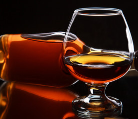 Glass of whiskey with bottle on dark background, selective focus
