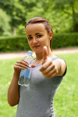  Young athletic girl drinks water after running in the park at sunrise