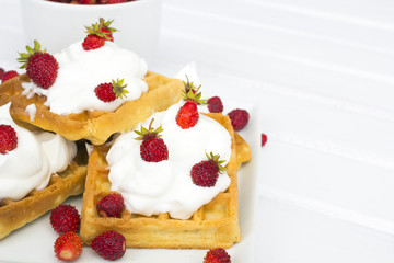 waffles with wild strawberries and whipped cream on white table
