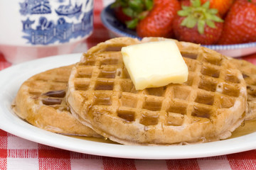 Waffles and Fruit Breakfast – Waffles with butter and syrup. Strawberries in the background.