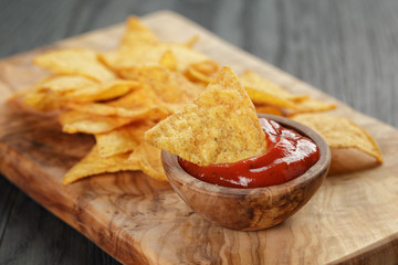 tortilla chips on olive board with tomato sauce, on wooden table