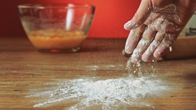 Baker hand throwing flour on the table, slow motion, 240 fps. Cooking and backing preparation. Food preparation on the red kitchen background. 