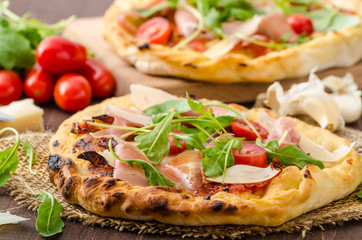 Italian pizza with parmesan cheese, prosciutto and arugula